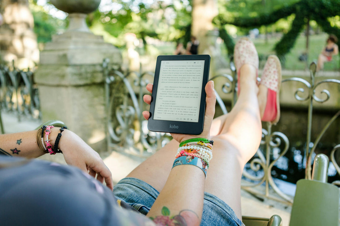 Woman with tattoos reading on her Kobo outside on a sunny day